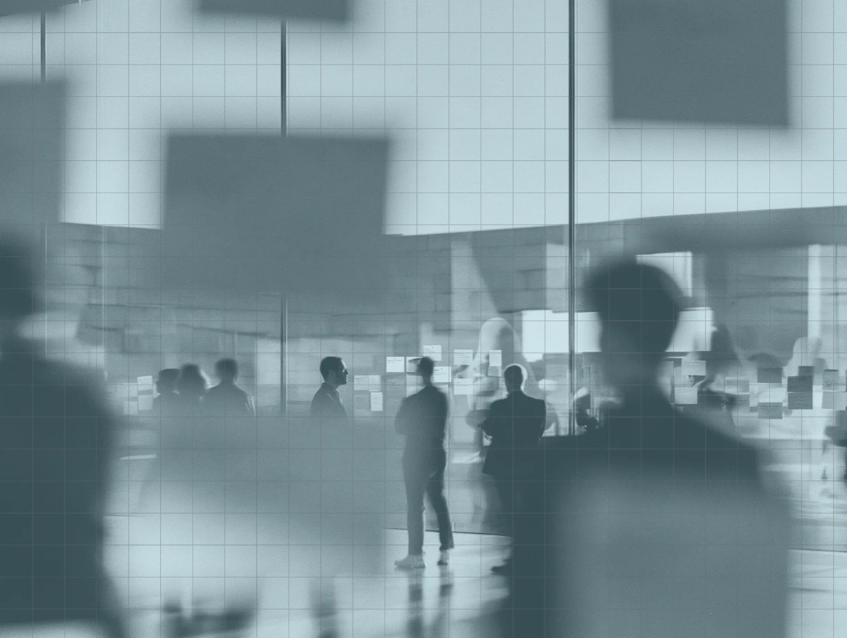 People standing and talking in a bright, open room, with notes stuck to the glass walls behind them, toned blue-grey under a faint grid.